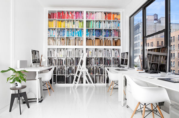 Artist studio with white walls and furniture and one large bookshelf filled with rainbow colored books