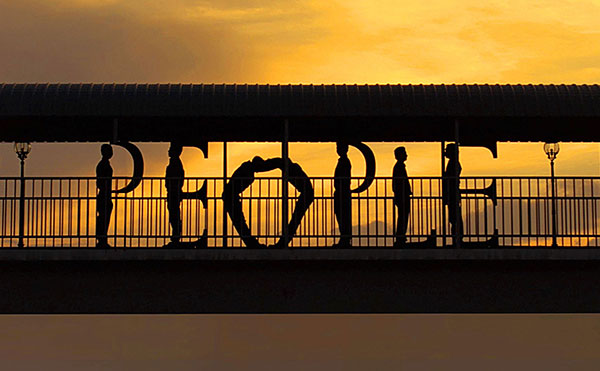 The word "people" made out of human beings standing on a bridge in front of a yellow sky