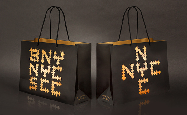 Two black gift bags with gold letters arranged in geometric patterns on the front