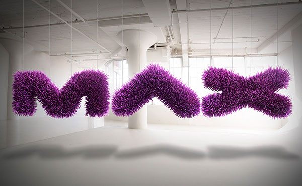 The 3D, purple, spiky letters MAX hang from the ceiling in an empty, white studio