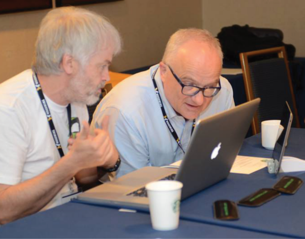 Two men, laughing and smiling, side by side looking at computer screen