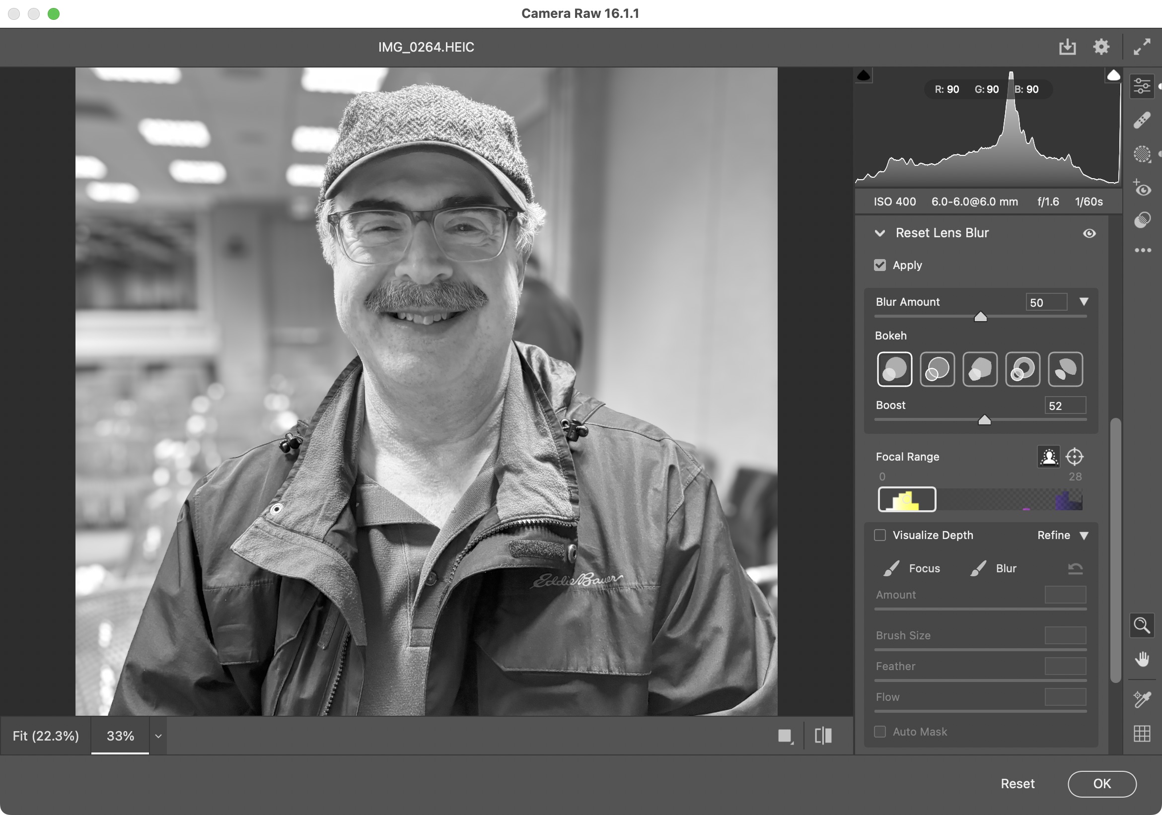 Screenshot of Adobe Camera Raw editing a black and white photo of a smiling man. The Lens Blur feature is enabled, blurring the area behind the man.