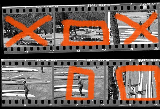 Photo of analog black-and-white film contact sheet, two strips with three frames each. In top row, first and third frame are crossed out with orange grease pencil. In top strip, second image is cropped horizontally with same grease pencil. Bottom strip, the second and third frames show cropping guidance with the grease pencil.