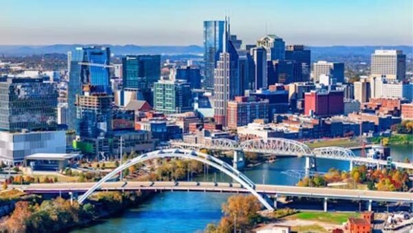 City skyline with a white arched bridge over a blue river, downtown buildings in the background.